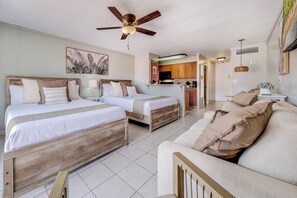 Une chambre d’hôtel avec deux lits, un ventilateur de plafond, un coin cuisine et un espace salon avec un canapé.