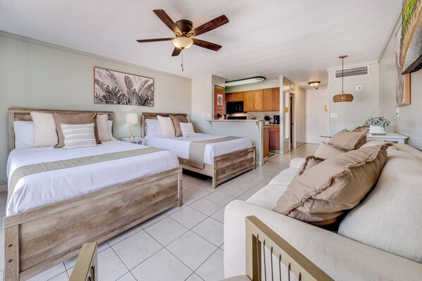 Habitación de hotel con dos camas, ventilador de techo, cocina y sala de estar con sofá.