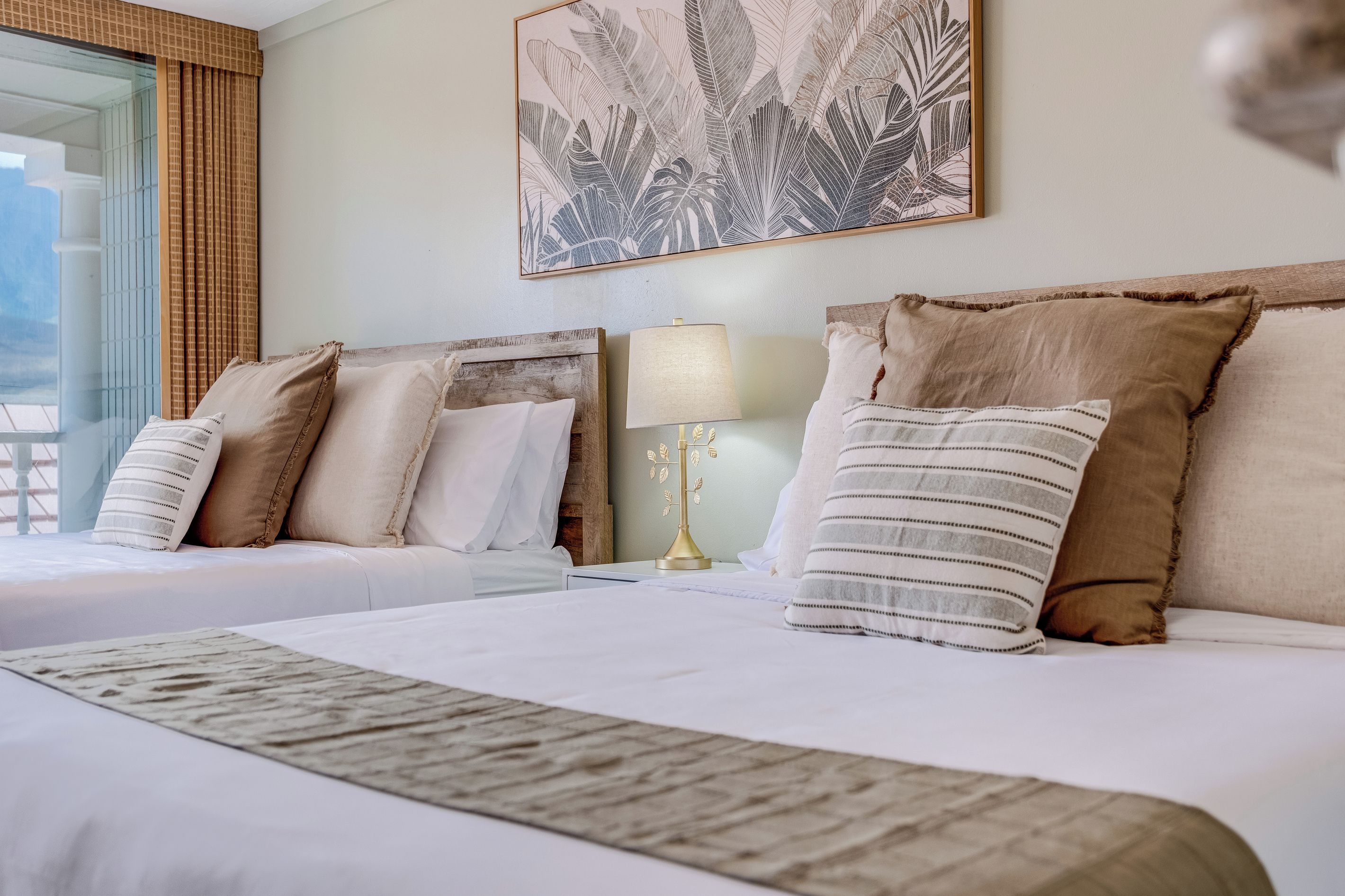 A hotel room with two beds, a large window, and a wall-mounted artwork.