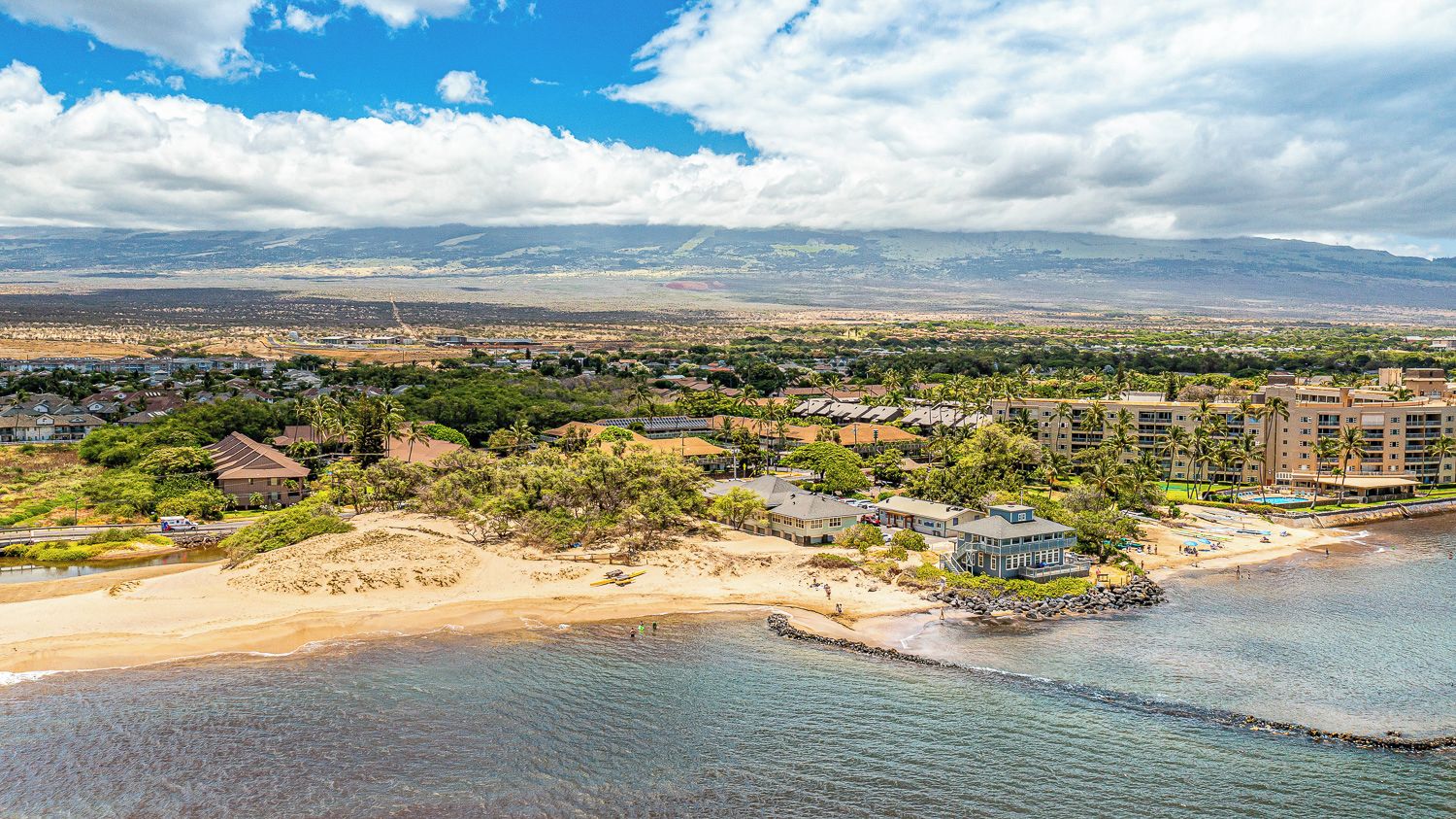 A coastal resort with beachfront properties, a sandy beach, and a view of distant mountains.