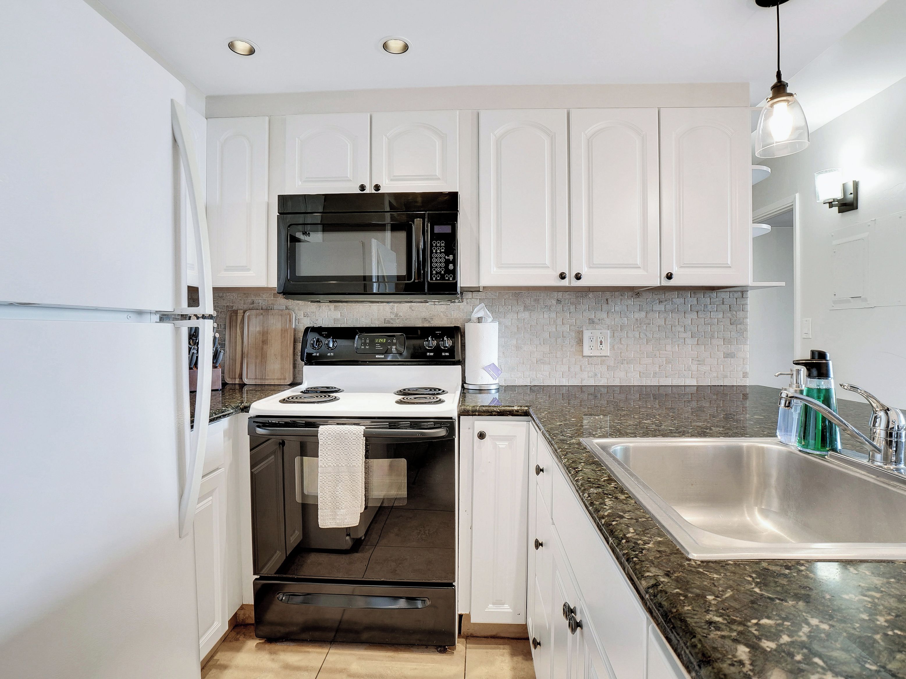 A modern kitchen with white cabinets, a black microwave, a stove, and a granite countertop.