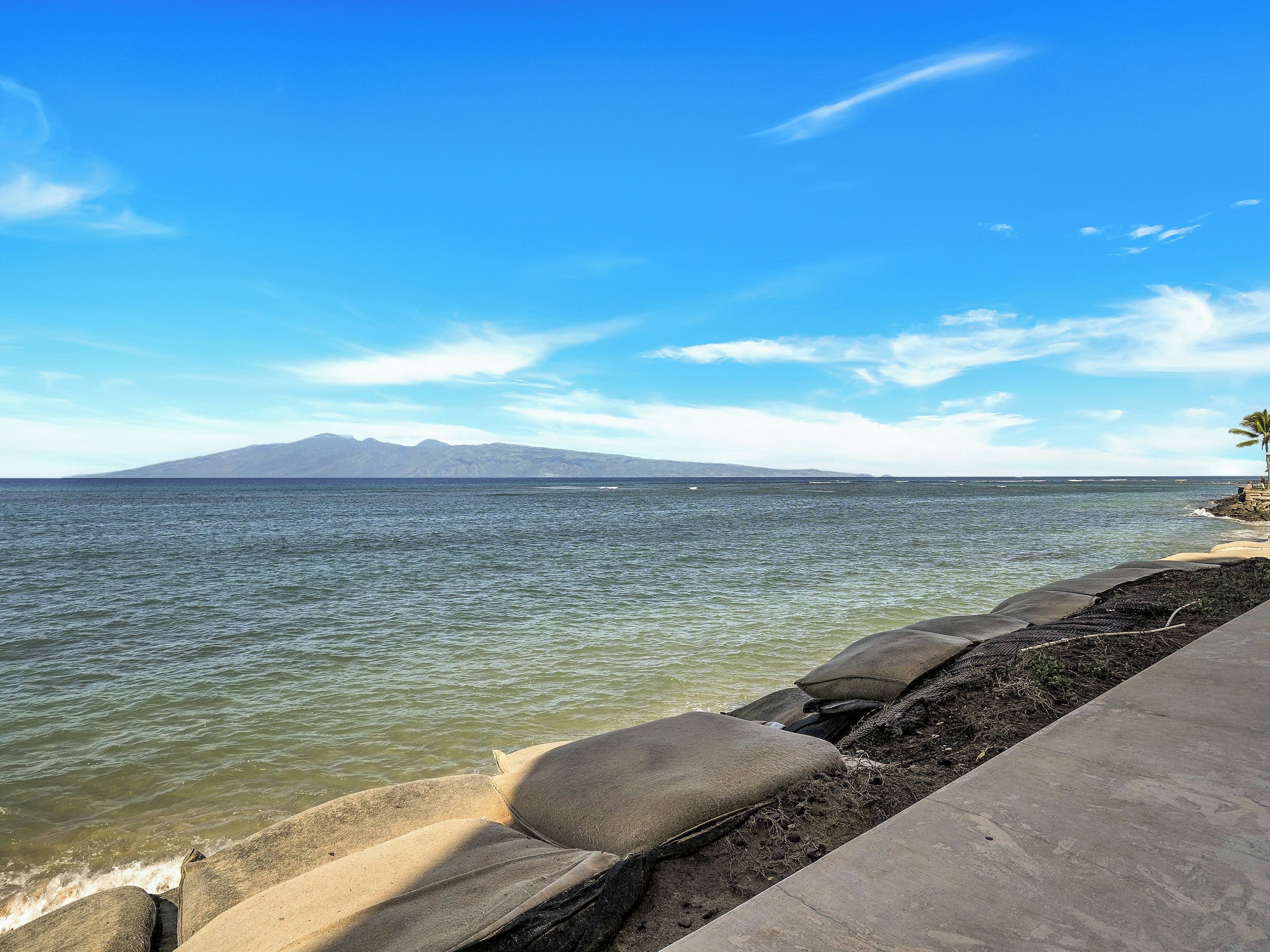 A coastal view with a clear sky, a rocky shoreline, and a distant mountain range.