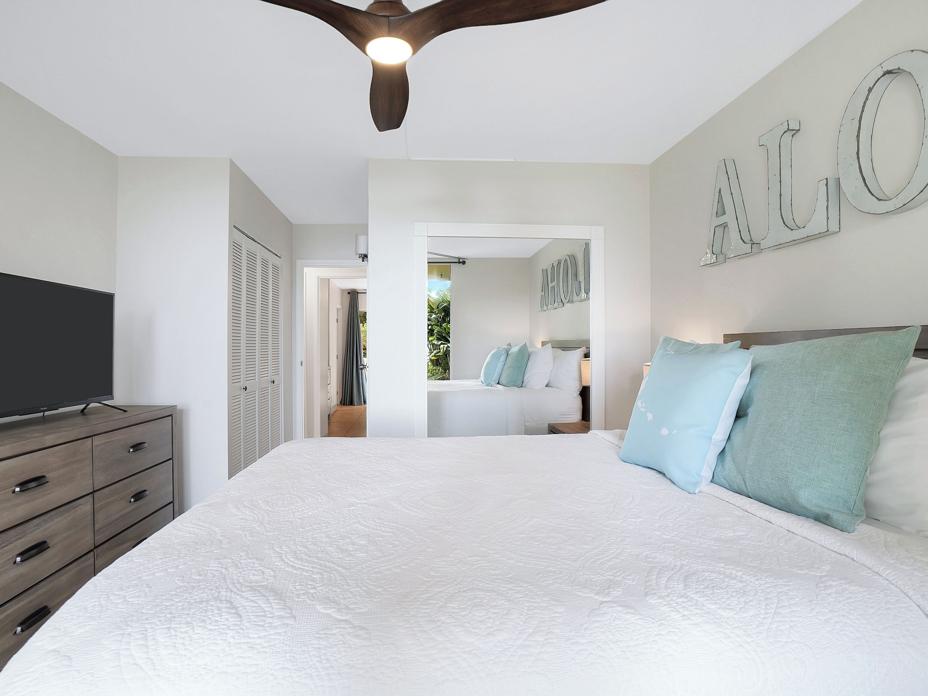 A bedroom with a large bed, a TV on a dresser, and a ceiling fan.