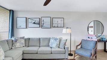 Een woonkamer met een grijze bank, een houten salontafel met tijdschriften, een vloerlamp en een ronde spiegel op een bijzettafeltje van hout.