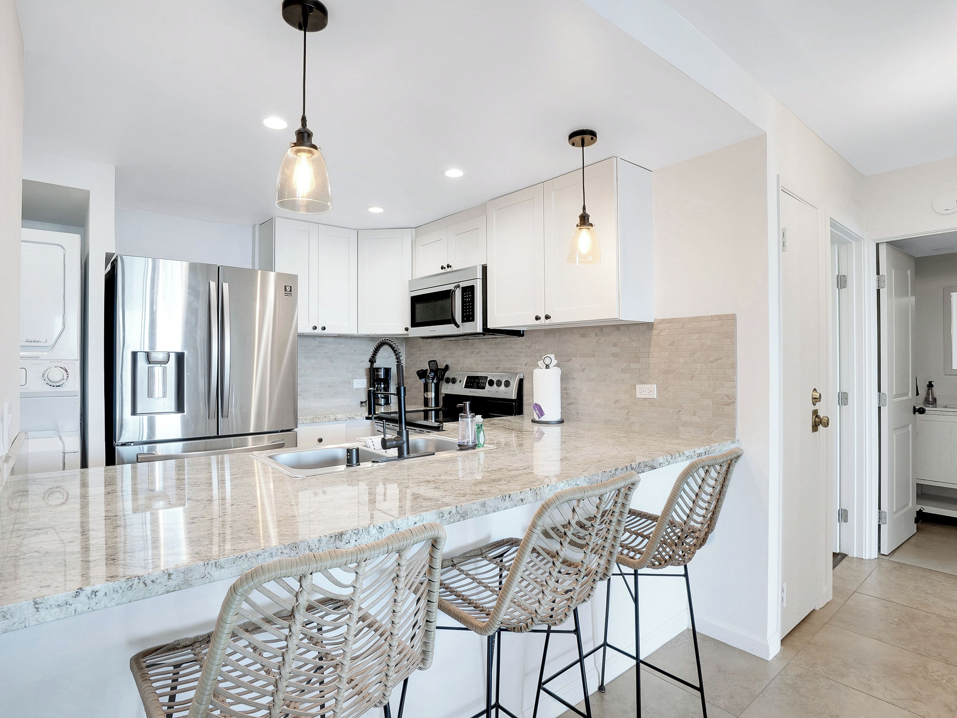 A modern kitchen with stainless steel appliances, a marble countertop, and wicker bar stools.