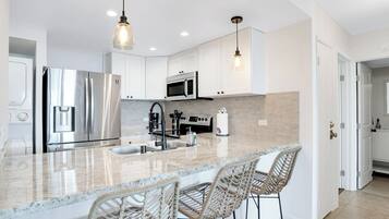 A modern kitchen with stainless steel appliances, a marble countertop, and wicker bar stools.