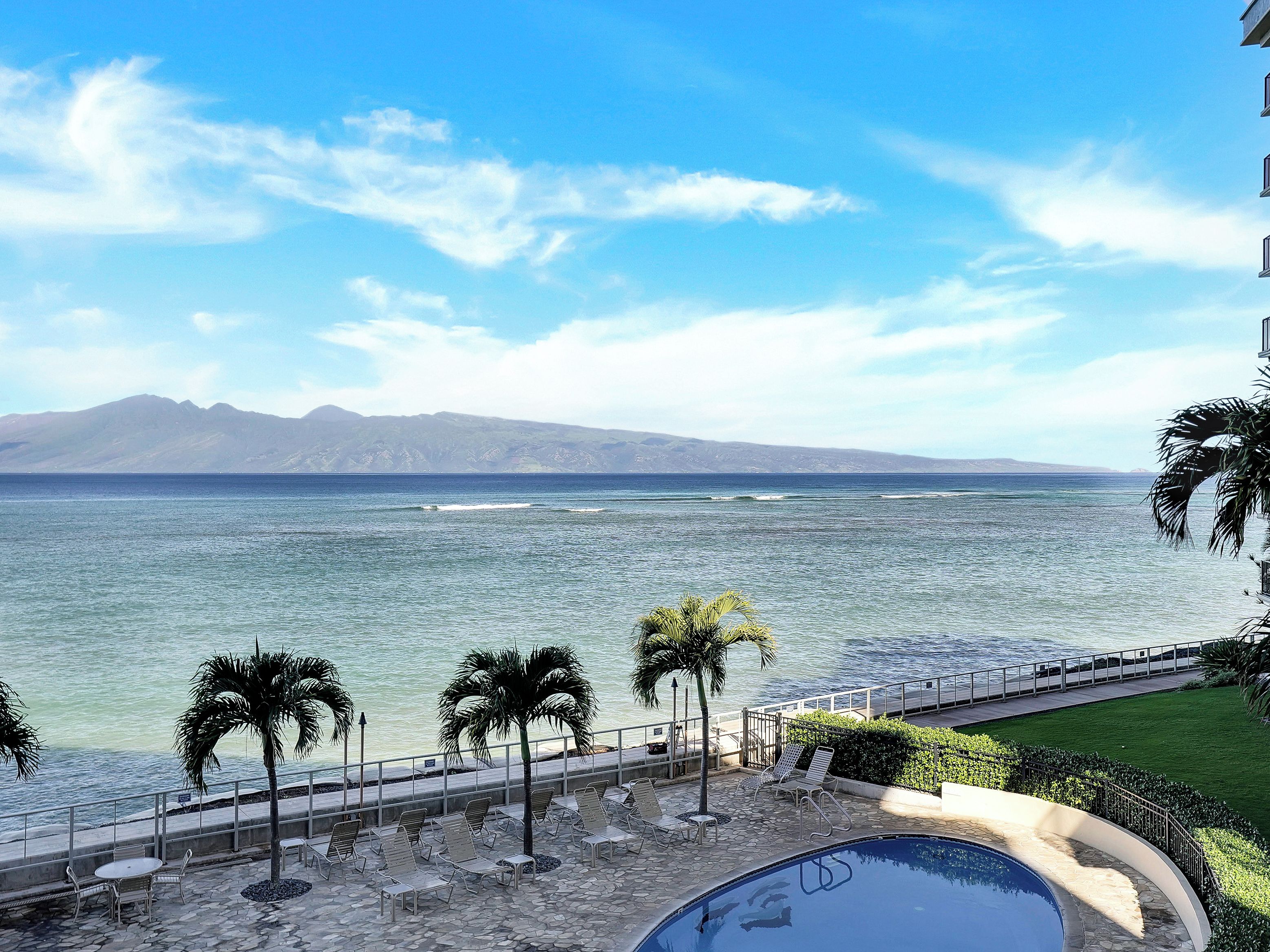 A poolside area with lounge chairs and a swimming pool, overlooking a body of water with mountains in the distance.