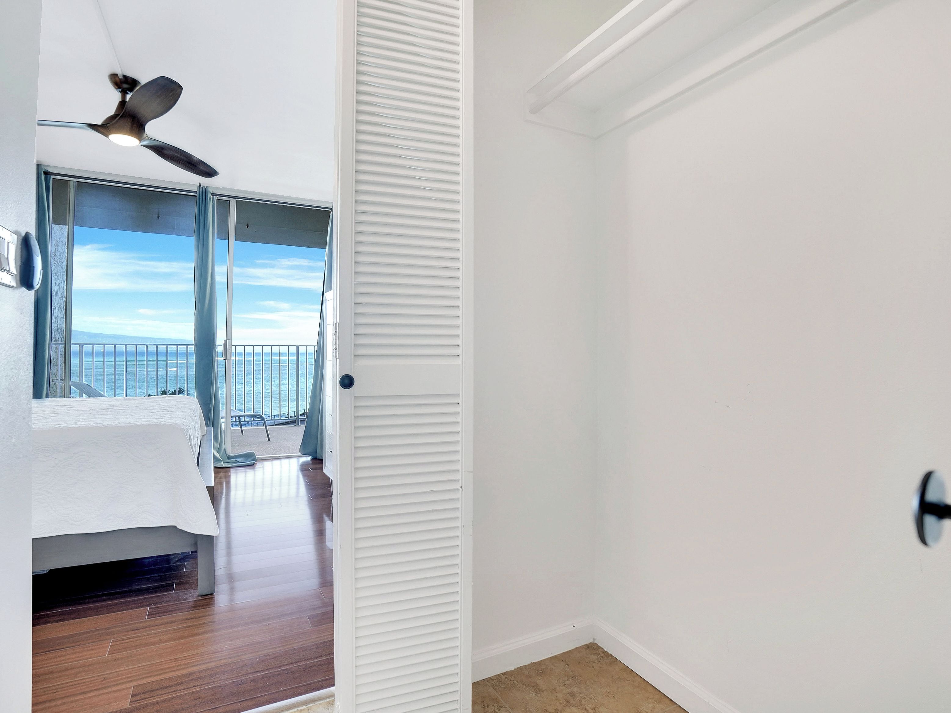 Een kamer met een bed, een plafondventilator, uitzicht op zee en een balkon met een hek.