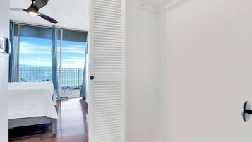 Een kamer met een bed, een plafondventilator, uitzicht op zee en een balkon met een hek.