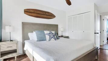 A bedroom with a bed, bedside tables, a ceiling fan, a wardrobe, and a view of the outside.