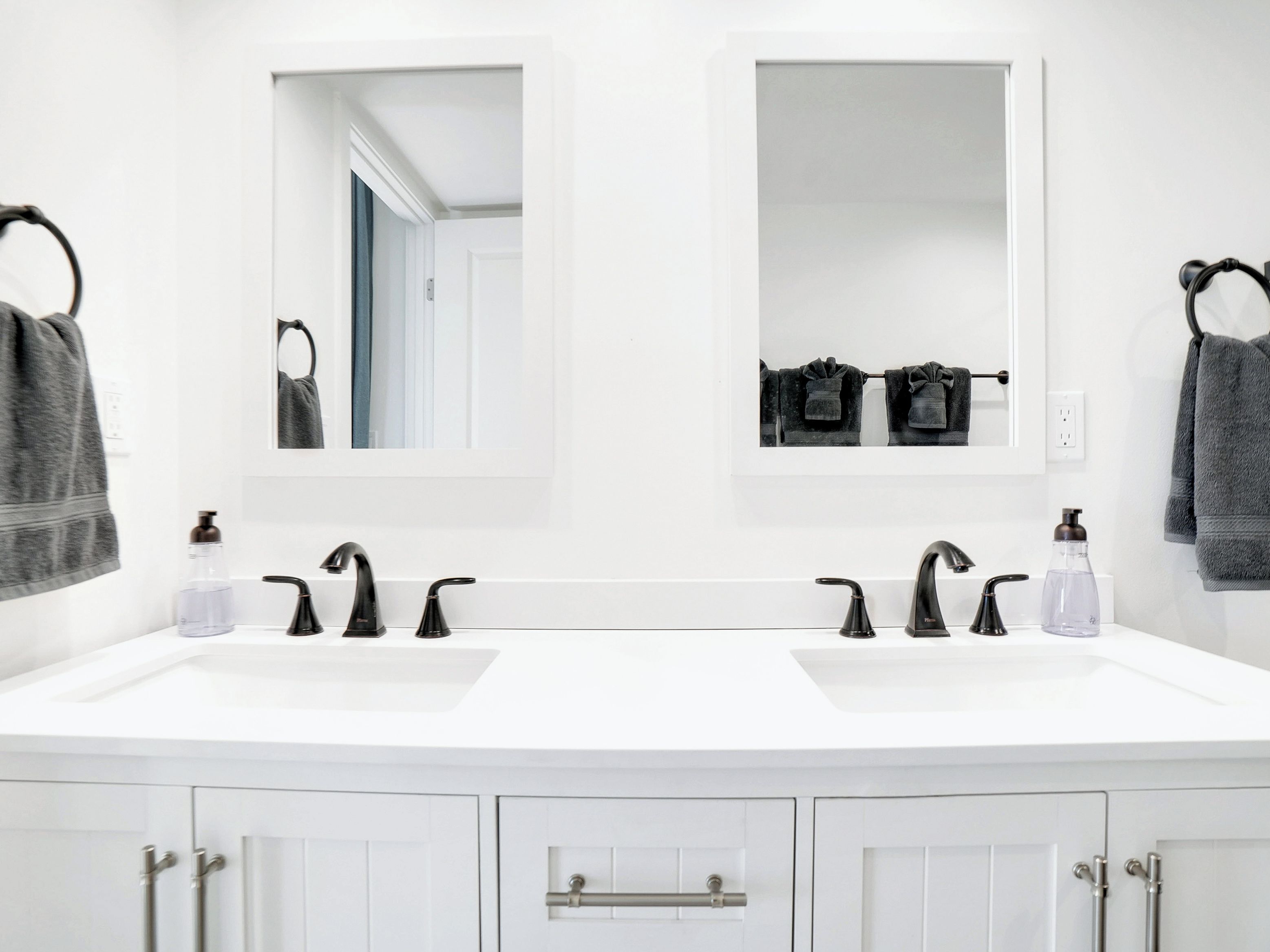 Une salle de bain moderne avec deux vasques, des robinets noirs et un miroir au-dessus de chaque vasque.