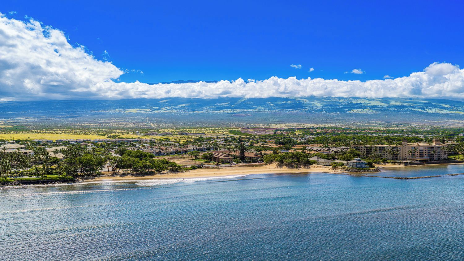 A coastal resort with beachfront properties, a marina, and a view of distant mountains.