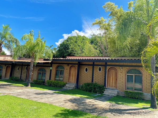 A row of brick buildings with arched windows and a tiled roof, surrounded by greenery. - Hotel Posada el Encanto (Chiconcuac)