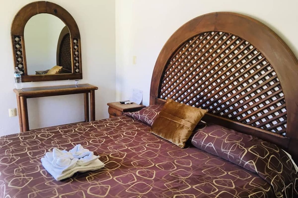 A bed with a patterned bedspread, a wooden headboard with a lattice design, a bedside table, and a mirror.