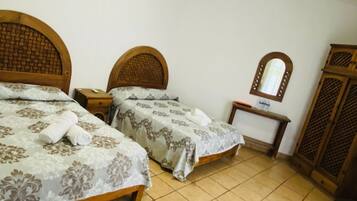 A hotel room with two beds, a bedside table, a mirror, a wardrobe, and an air conditioning unit.