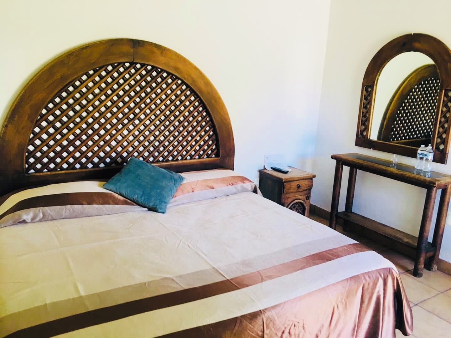 Una cama con cabecera de madera, una mesita de noche, un espejo y una botella de agua.
