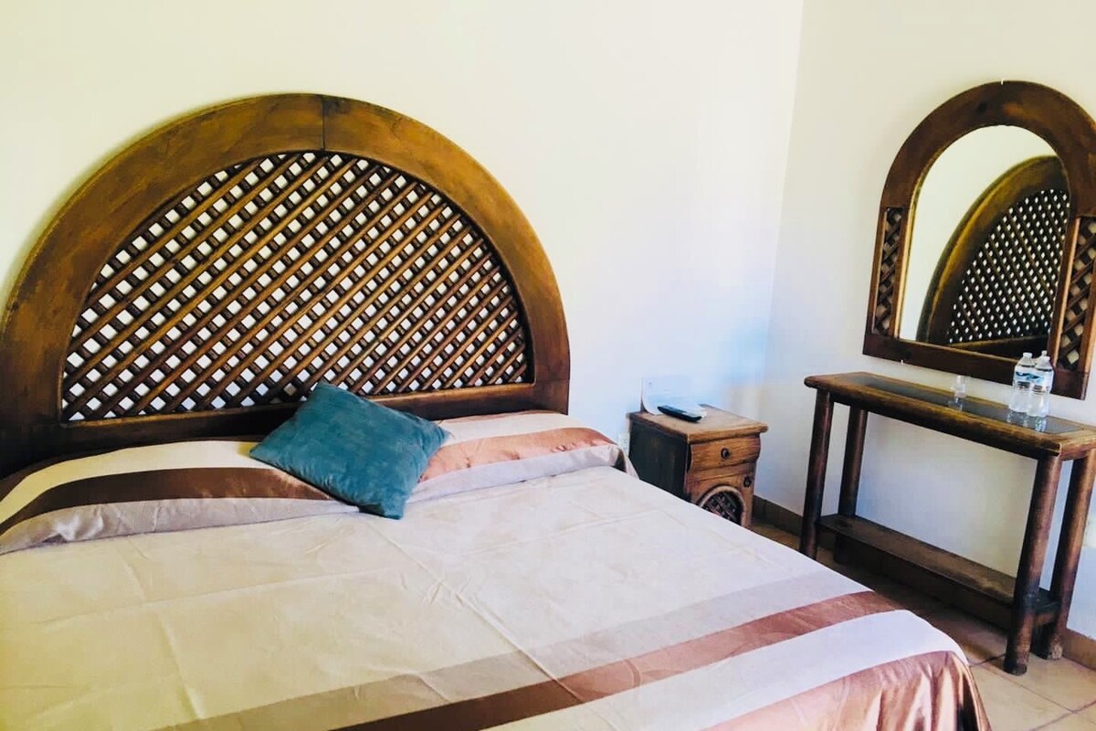 A bed with a wooden headboard, a bedside table, a mirror, and a water bottle.