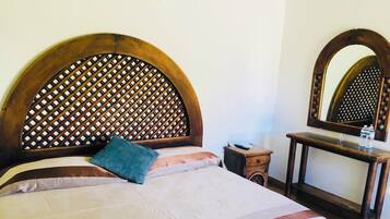 Una cama con cabecera de madera, una mesita de noche, un espejo y una botella de agua.