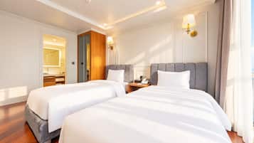 Habitación de hotel con dos camas, una mesita de noche con lámpara, un espejo y vista al mar.