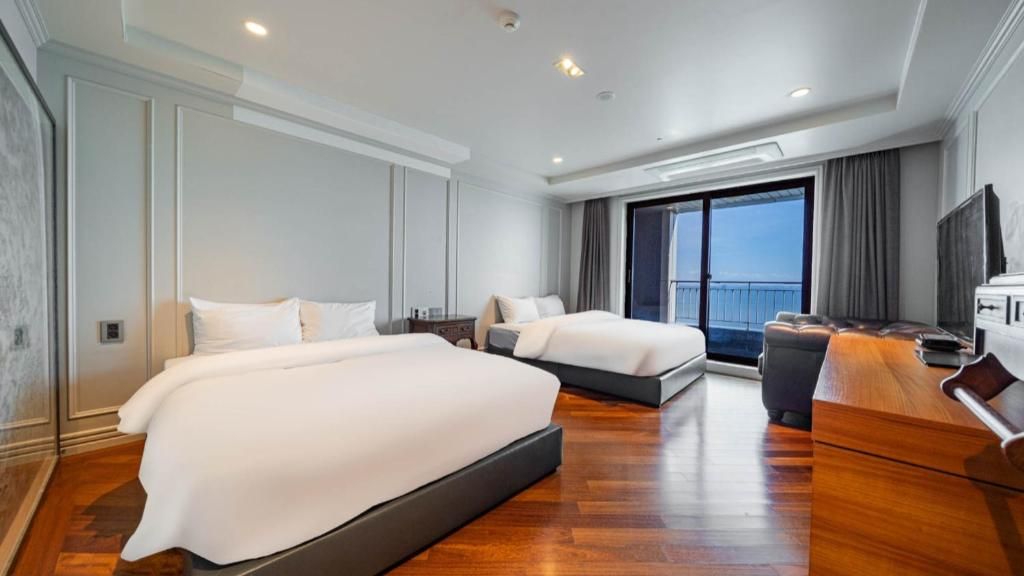 A modern hotel room with two beds, a large window, and a flat-screen TV.