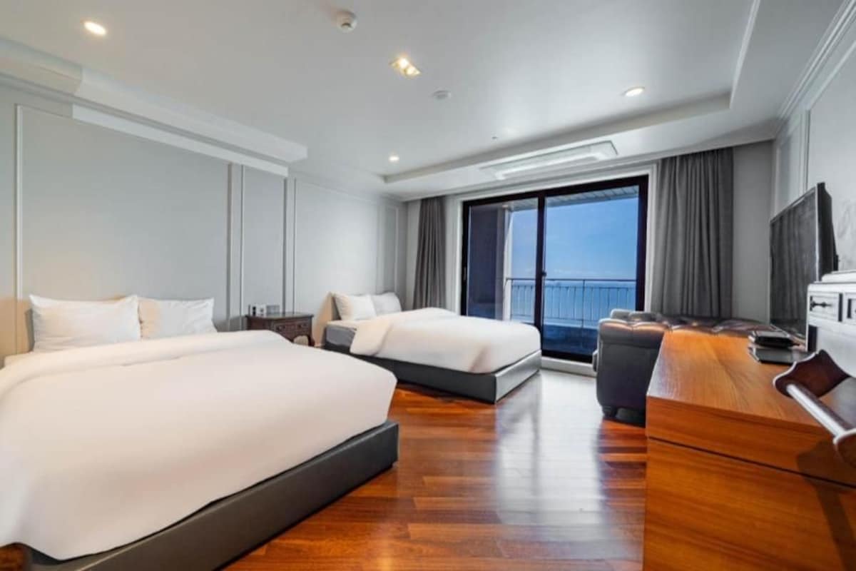 A modern hotel room with two beds, a large window, and a flat-screen TV.