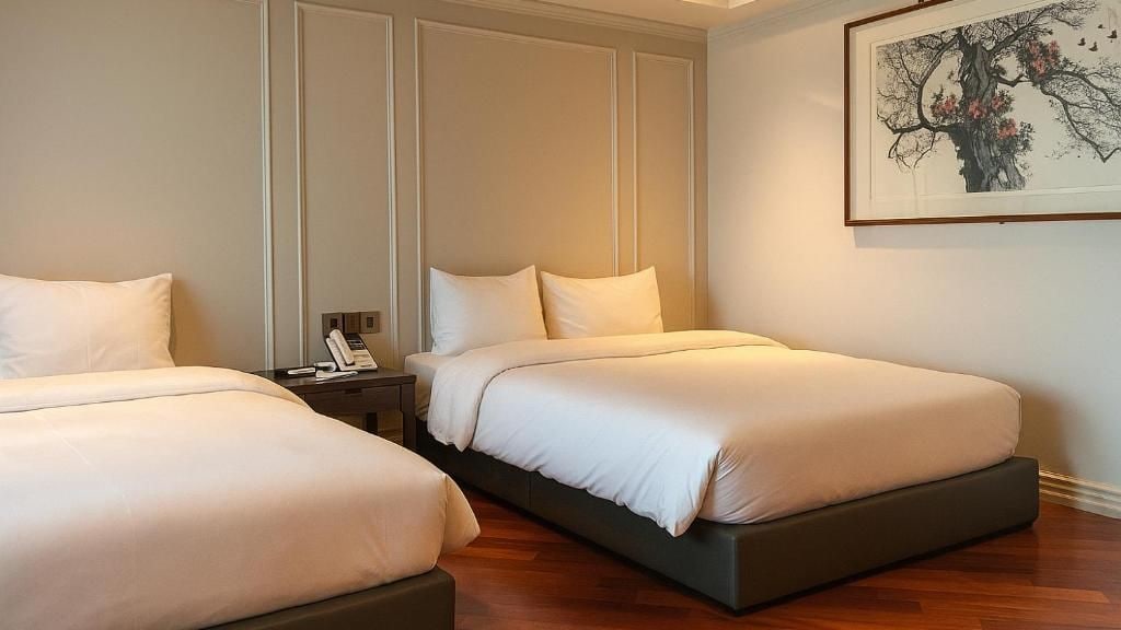 Habitación de hotel con dos camas, una mesita de noche con teléfono y una obra de arte enmarcada en la pared.