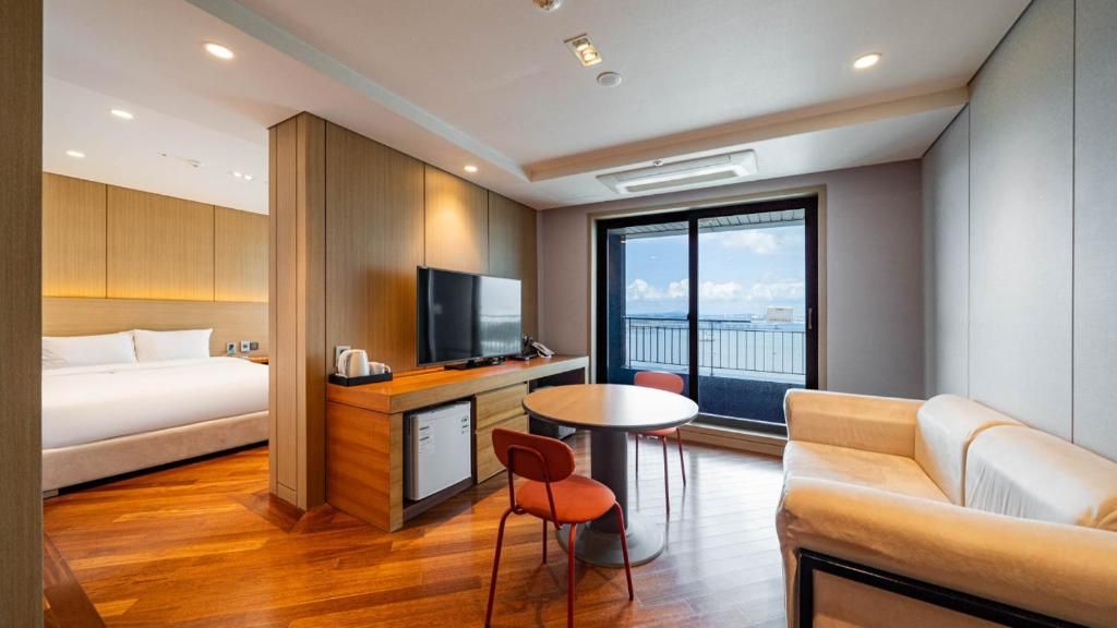 Una habitación de hotel moderna con cama, escritorio, televisión, mesa de comedor con sillas y un sofá.