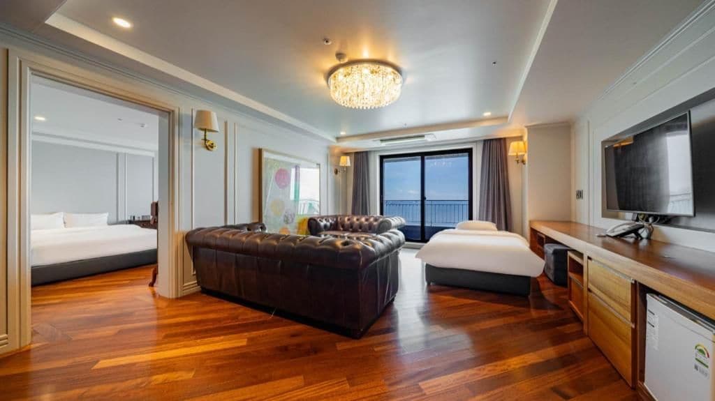 A hotel room with a large bed, a sofa, a desk with a television, and a balcony with a view.
