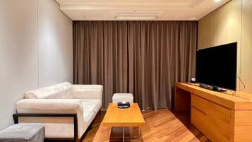 A hotel room with a sofa, a small table, a TV, and a wooden cabinet.