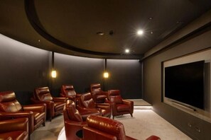 A dark room with leather recliners arranged in a semi-circle, a large flat-screen TV, and two wall-mounted lights. - Queen's Wharf Residences Luxury 2 Beds 1 Car (Brisbane)