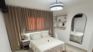 Una camera da letto con un letto, un comodino, tende, uno specchio e uno scaffale con oggetti decorativi.
