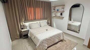 Un dormitorio con cama, mesita de noche, cortinas, un espejo y estante con adornos.
