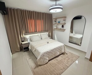 Un dormitorio con cama, mesita de noche, cortinas, un espejo y estante con adornos.