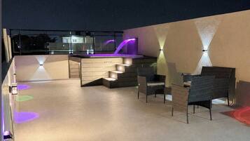 Una terraza al aire libre con zona de bar, asientos e iluminación ambiental.