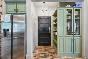 Una cocina con un refrigerador de acero inoxidable, una puerta negra y gabinetes verdes.