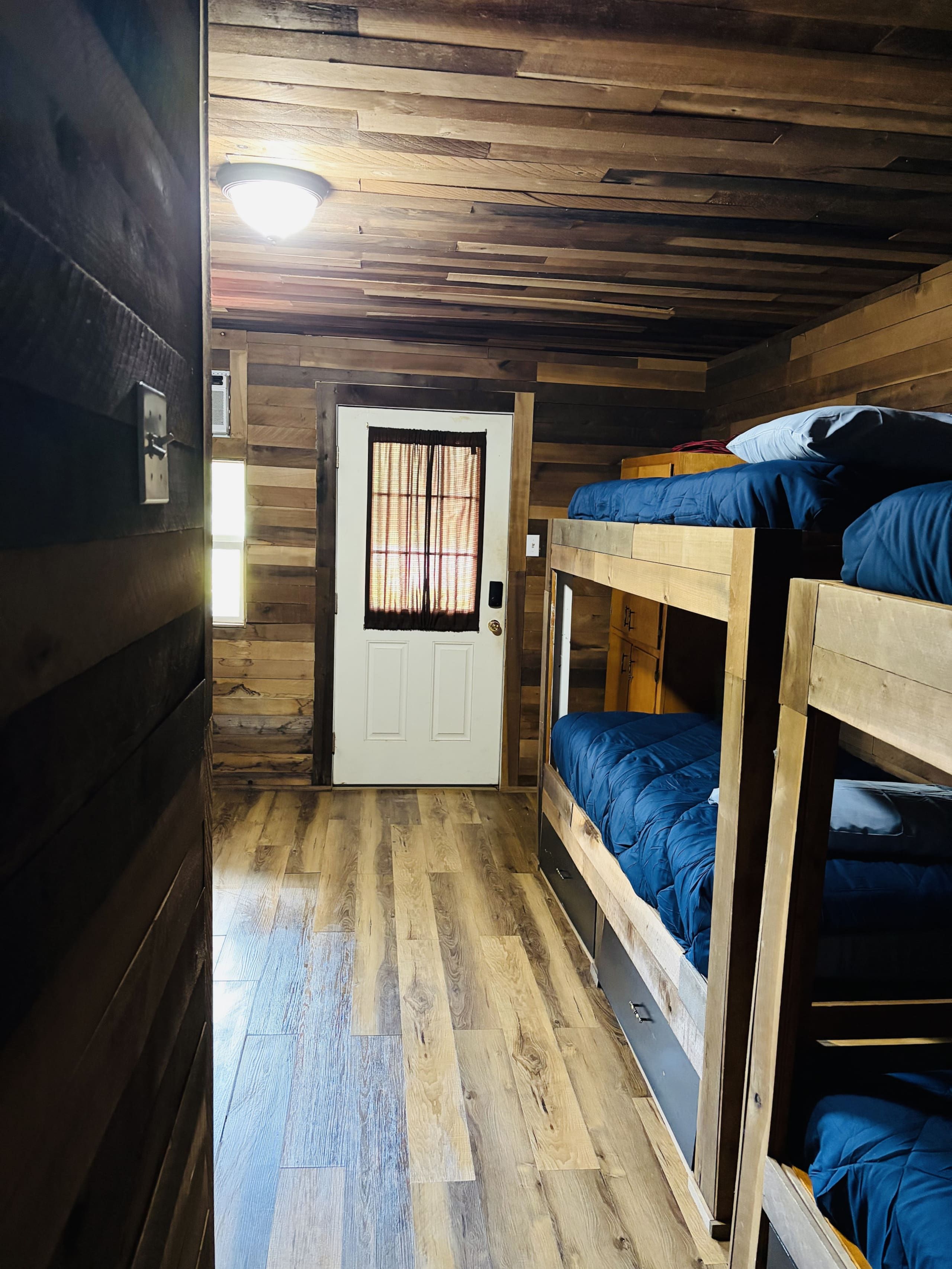 Un couloir étroit aux murs en bois et une porte dotée d’une fenêtre. On y trouve des lits superposés avec du linge de lit bleu.