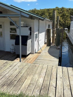 A wooden dock leading to a white building with a green roof, a gas tank, and a water pump.