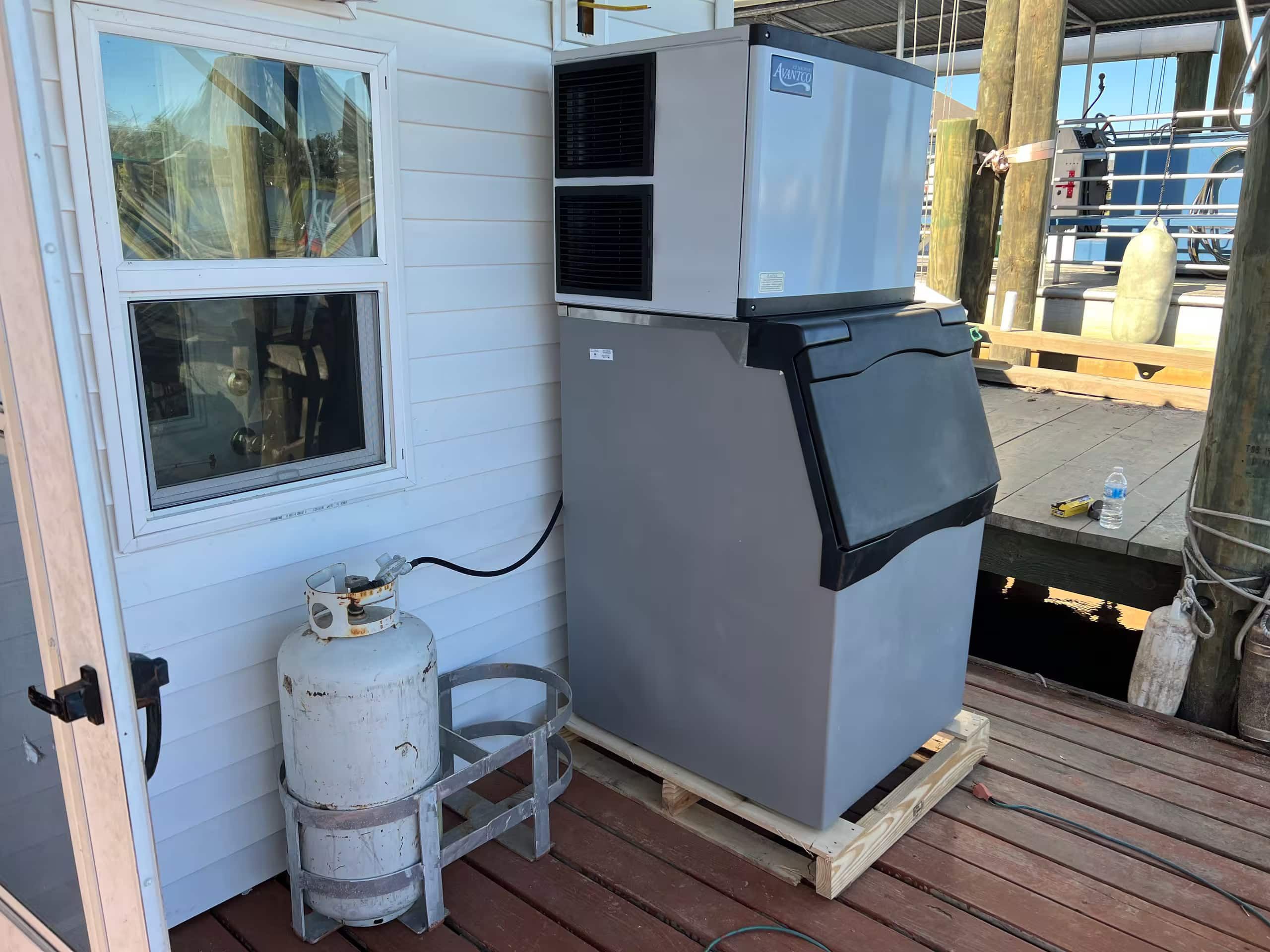 A compact room with a window, a large gray refrigerator, and a white propane tank.