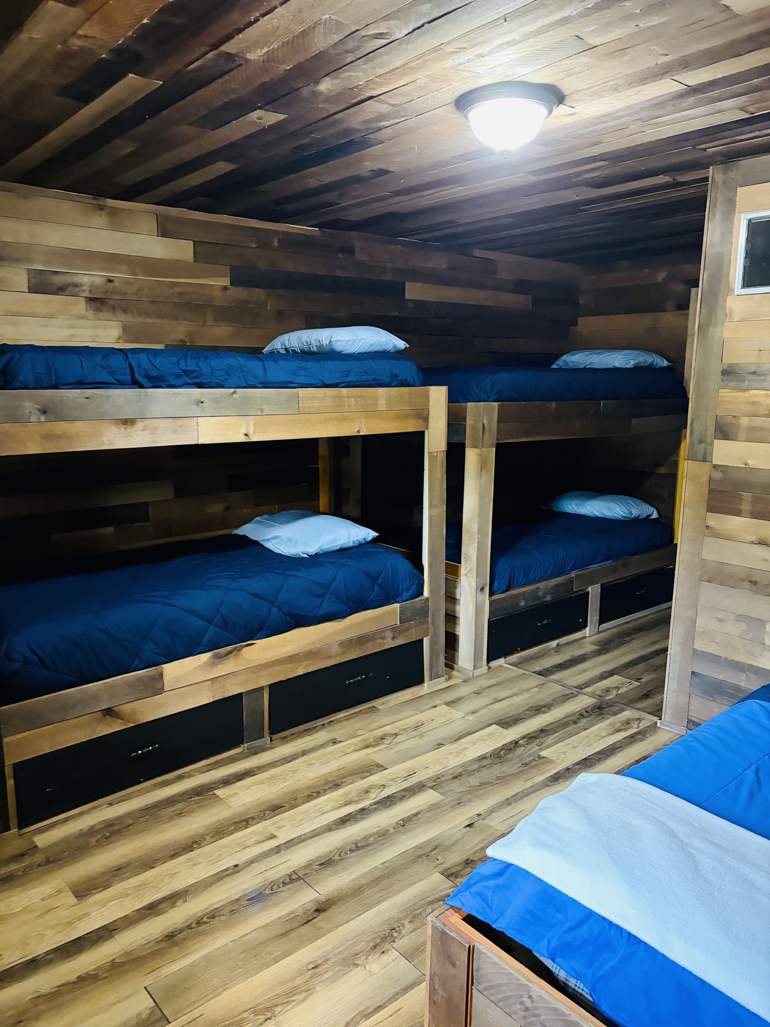 Een slaapkamer met stapelbedden, houten wanden en vloeren, met drie stapelbedden voorzien van blauw beddengoed.