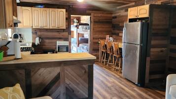 L’intérieur d’un chalet rustique est doté d’un plafond en bois, d’un coin cuisine avec un réfrigérateur, d’une table à manger avec des chaises et d’un canapé agrémenté d’un coussin.