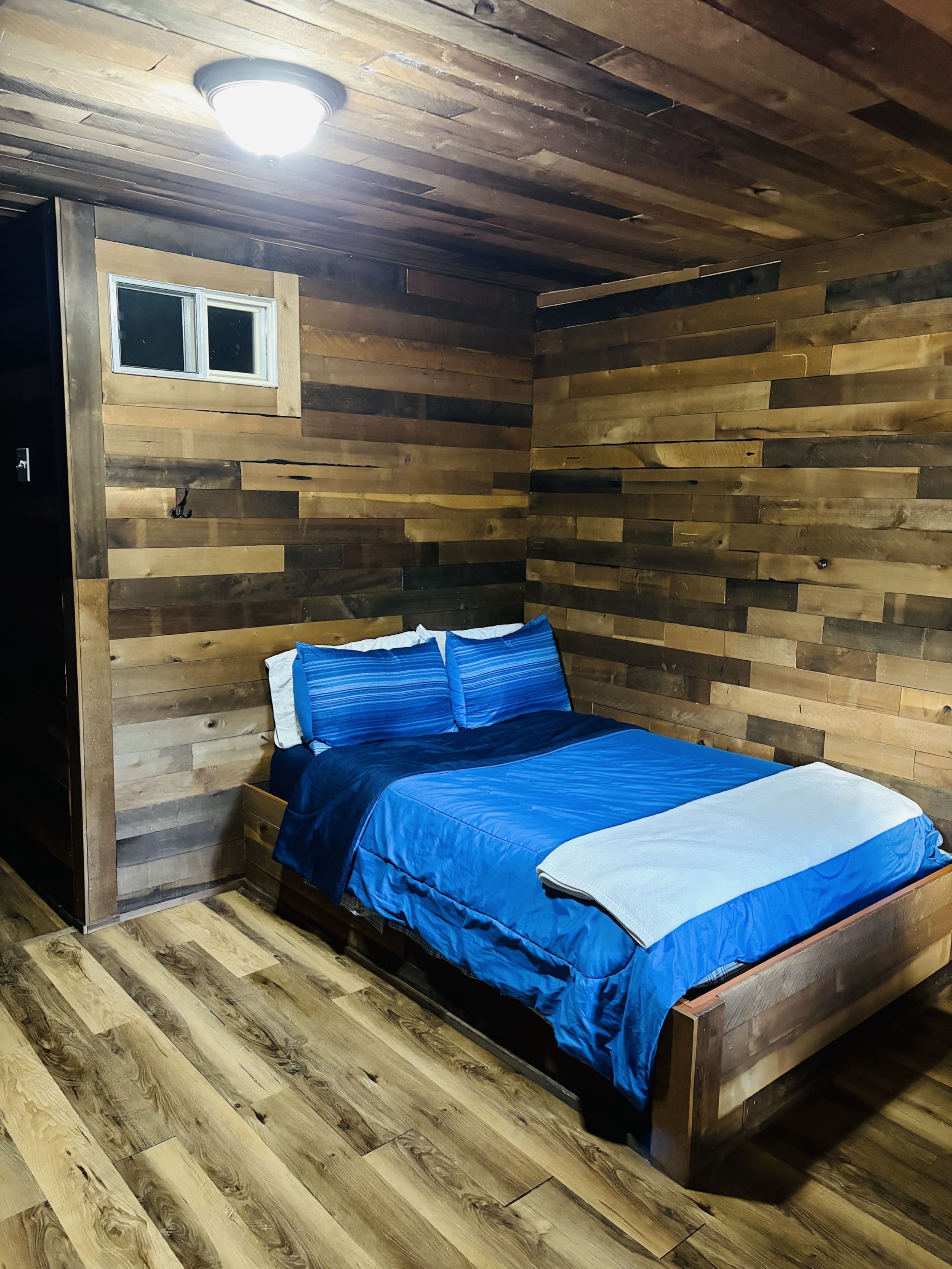 Ein Einzelbett mit blauer Bettwäsche in einem Zimmer mit Holzwänden und einer geneigten Decke.