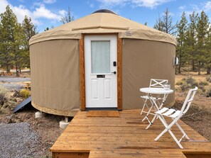 A yurt with a wooden door, a small porch with a table and chairs, and a clear sky in the background. - Lumberjack 20' Yurt, King Bed Glamping in Bend (Bend)