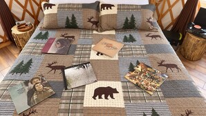 Ein Bett mit einem Patchwork-Quilt mit Tiermotiven, umrahmt von einem Holz-Kopfteil und Nachttischen mit Dekoration.