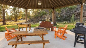 Eine Terrasse im Freien mit einem Holztisch, Bänken, einem Grill und einer Feuerstelle.
