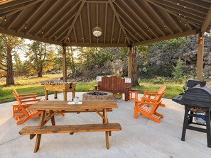 An outdoor patio with a wooden table, benches, a barbecue grill, and a fire pit. - Lumberjack 20' Yurt, King Bed Glamping in Bend (Bend)