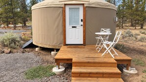 Eine Jurte mit einer Holzterrasse und einem Tisch mit Stühlen davor.