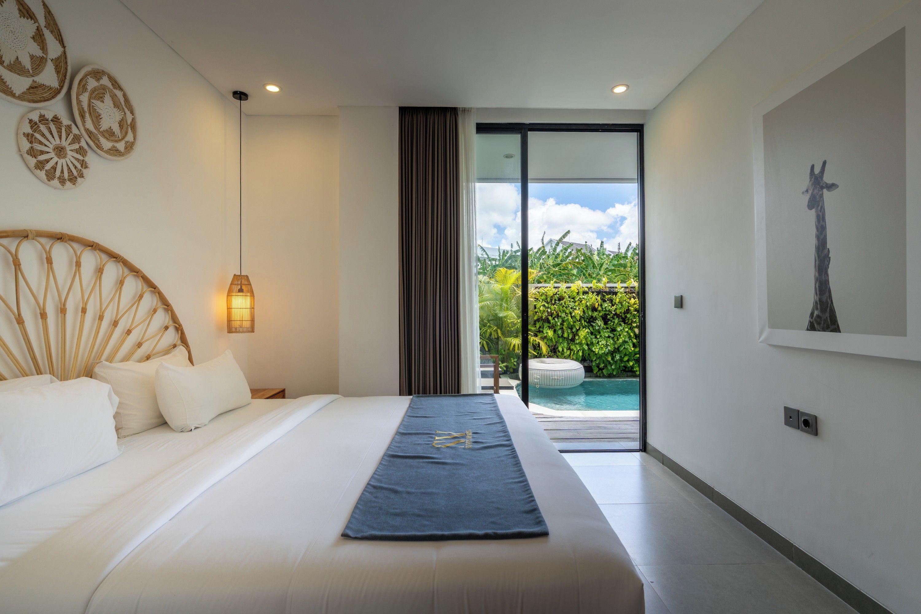 A modern bedroom with a large bed, a view of a swimming pool, and a giraffe painting on the wall.