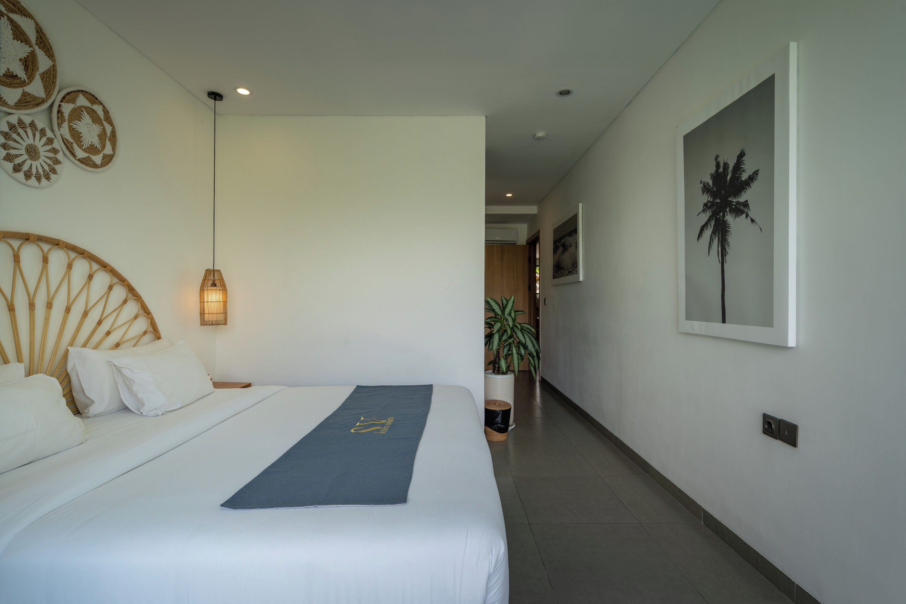 Habitación de hotel con una cama, una lámpara de noche, aire acondicionado instalado en la pared, una planta en maceta y un cuadro enmarcado.
