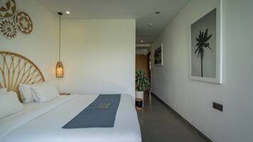 Habitación de hotel con una cama, una lámpara de noche, aire acondicionado instalado en la pared, una planta en maceta y un cuadro enmarcado.