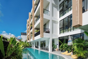 Un hotel de varios pisos con piscina, asientos al aire libre y balcones.